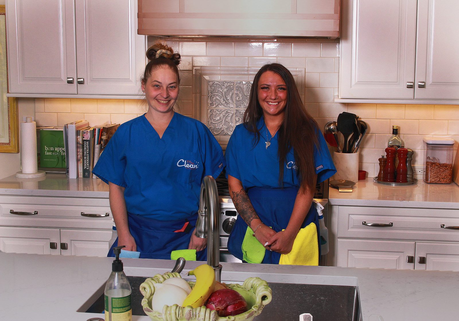 Two Mrs. Clean Pittsburgh team members in branded uniforms, smiling in a client's kitchen